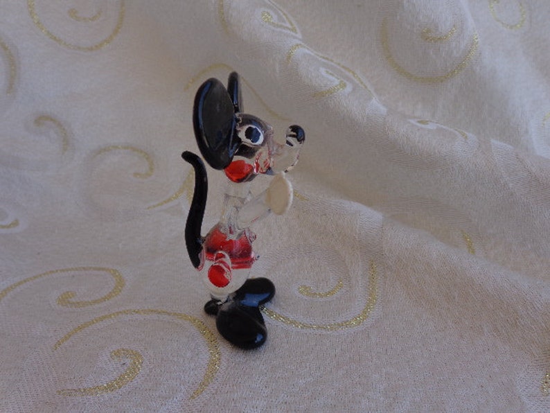 May include: A black and white glass figurine of a cartoon mouse with red accents. The mouse is standing on its hind legs with its tail curled behind it.