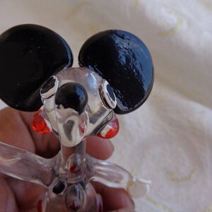 May include: A clear glass figurine of a mouse with black ears and red accents. The mouse is standing on its hind legs with its front paws raised.