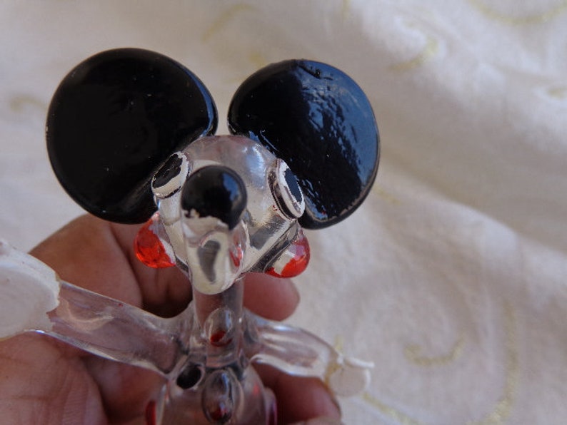 May include: A clear glass figurine of a mouse with black ears and red accents. The mouse is standing on its hind legs with its front paws raised.
