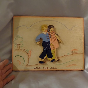 May include: A vintage wooden wall art piece depicting Jack and Jill going up the hill. The figures are painted in blue, pink, and yellow, and the background is painted in shades of brown and green. The text "Jack and Jill" is written at the bottom of the piece.
