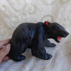 May include: Black rubber toy bear with an open mouth, standing on a white surface.
