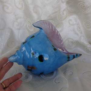 May include: A blue glass seashell with black and green spots and a pink iridescent lip. The seashell is a decorative object.