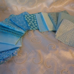 May include: A collection of 12 blue fabric squares with various patterns, including geometric, floral, and polka dot designs. The squares are arranged in a semi-circle on a white background with a gold swirl pattern.