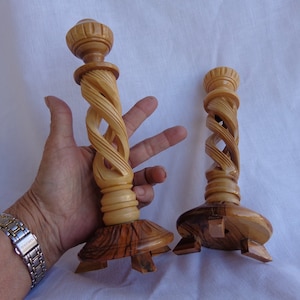 May include: Two wooden candle holders with a spiral design. The holders are made of light brown wood and have a base with four legs.
