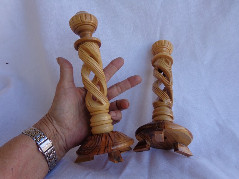 May include: Two wooden candle holders with a spiral design. The holders are made of light brown wood and have a base with four legs.