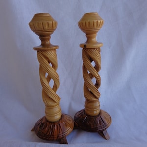May include: A pair of wooden candle holders with a twisted design. The holders are made of light brown wood and have a dark brown base.