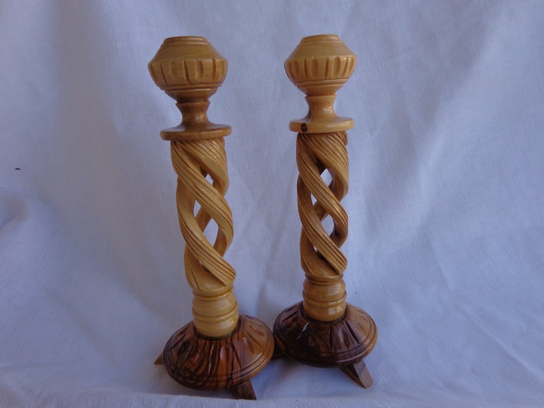 May include: A pair of wooden candle holders with a twisted design. The holders are made of light brown wood and have a dark brown base.