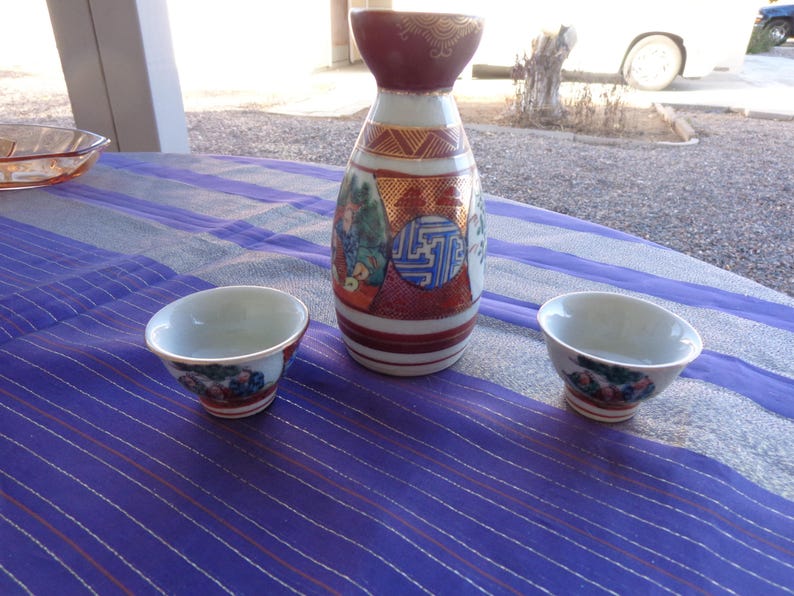 two cups and sake container Enlarge for detail Vintage Sake set Signed Scene has flower on one side and Four Japanese Men on other