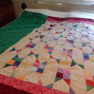 May include: A patchwork quilt featuring a repeating geometric star pattern in various colors including red, blue, yellow, and green on a cream background. The quilt has a wide dark red border and a solid green section on one side of the fabric.