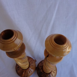 May include: A pair of wooden candle holders with a natural wood finish. The holders are intricately carved and have a unique, rustic look.