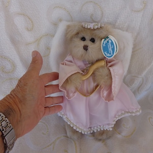 May include: A plush angel bear wearing a pink dress and holding a gold harp. The bear has a white halo and a tag that reads "The Bridgewater Collection".