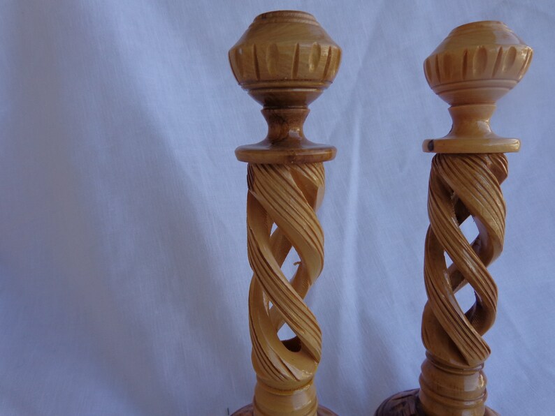 May include: Two wooden candle holders with a spiral design. The holders are made of light brown wood and have a simple, elegant design.