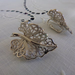 May include: A pair of silver filigree earrings shaped like leaves. The earrings have a delicate, intricate design and are perfect for adding a touch of elegance to any outfit.