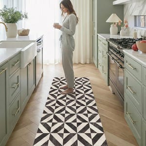 Könnte beinhalten: Eine schwarz-weiß geometrisch gemusterte Küchenmatte. Die Matte ist rechteckig und weist ein sich wiederholendes Dreieckmuster auf. Die Matte liegt auf einem Holzboden in einer Küche.