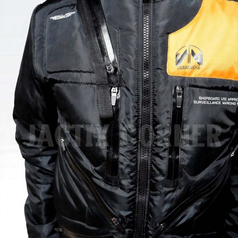 May include: Black jacket with a zipper closure, multiple pockets, and a yellow and orange accent on the upper right chest. The jacket has the text "DRAWERIDGE" and "SHIPBOARD USE APPROVAL SURVEILLANCE MARKING" printed on it. The jacket has a black strap with a silver zipper.