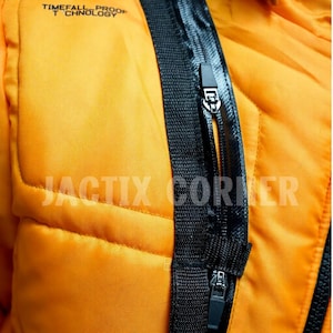 May include: Close-up of a bright orange jacket with black zippers and trim. The jacket has a quilted pattern and the text "TIMEFALL PROOF TECHNOLOGY" is printed at the top. The text "JACTIX CORNER" is printed at the bottom.