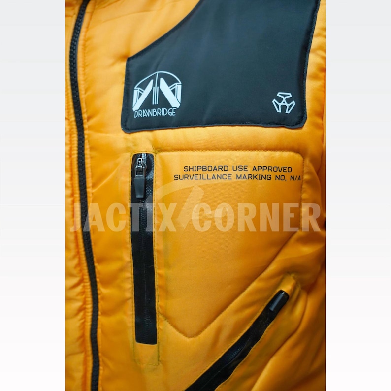 May include: Close-up of a yellow and black jacket with a zipper and a pocket. The jacket has the text "DRAWBRIDGE" and "ACTIX CORNER" printed on it. The jacket also has the text "SHIPBOARD USE APPROVED SURVEILLANCE MARKING NO, N/A".