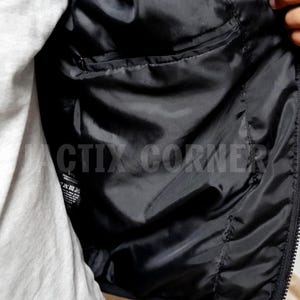 May include: Close-up of the inside of a black jacket. The interior lining is smooth and shiny, with a small pocket visible. The jacket is partially unzipped, revealing a gray shirt underneath. The text "CTIX CORNER" is visible.