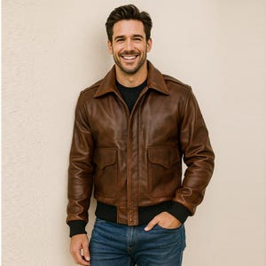 Könnte beinhalten: Braune Lederjacke mit Kragen, zwei Vordertaschen und schwarzen gerippten Bündchen und Saum. Die Jacke wird mit einem schwarzen Hemd und blauen Jeans getragen. Die Jacke hat einen klassischen, Vintage-Stil.