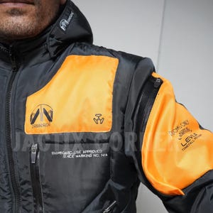 May include: Black and orange jacket with a hood. The jacket features orange panels on the chest and arm, with the text "DRAWBRIDGE" and "DOOMS ONLY". It has multiple zippers and a logo on the hood.