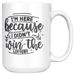 May include: White ceramic mug with a large handle. The mug features the text "I'M HERE because I DIDN'T win the LOTTERY" in black script and block letters, with decorative leaf accents.