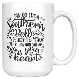 May include: White ceramic mug with a large handle. The mug features black text that reads "I CAN GO FROM Southern Belle TO GHETTO THUG - FASTER THAN YOU CAN SAY - Bless your heart." Stars and floral designs accent the text.