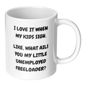 May include: White ceramic mug with a black humorous quote: "I LOVE IT WHEN MY KIDS SIGH. LIKE, WHAT AILS YOU MY LITTLE UNEMPLOYED FREELOADER?" The mug has a curved handle and is suitable for hot or cold beverages.