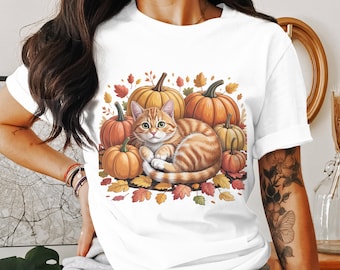 May include: White t-shirt featuring a cartoon illustration of a ginger tabby cat curled up among pumpkins and autumn leaves. The pumpkins are orange and the leaves are red, orange, and yellow.
