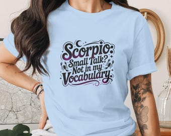 May include: Pale blue t-shirt with a graphic that reads "Scorpio: Small Talk? Not in my Vocabulary." The design incorporates a moon, stars, and scorpion symbols. This is a casual wear item.