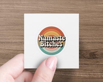 Może przedstawiać: Okrągła naklejka z napisem "Namaste Bitches" w stylu retro. Projekt ma tło w kształcie tęczy z odcieniami pomarańczu, brązu i turkusu. Naklejka znajduje się na białym kwadracie.