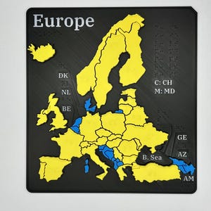 May include: A black and yellow Europe map puzzle with raised country outlines and Braille text. The word "Europe" is printed in white at the top. Country abbreviations are also visible.