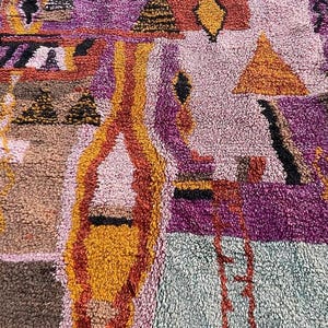 May include: A colorful, textured rug with a geometric design. The rug features a mix of colors, including purple, orange, yellow, and brown. The design includes triangles, diamonds, and other shapes. The rug is made of a thick, woven material.