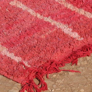 May include: Close-up of a red and white patterned rug with a textured surface. The rug has a fringe along the edge. The rug is made of a thick, woven material. The rug is likely used as a floor covering.