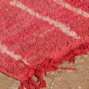 May include: Close-up of a red and white patterned rug with a textured surface. The rug has a fringe along the edge. The rug is made of a thick, woven material. The rug is likely used as a floor covering.