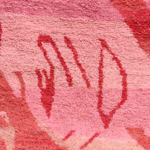 May include: Close-up of a pink and red rug with a textured surface. The rug features abstract shapes in varying shades of pink and red, creating a vibrant and artistic design. The rug's design is a mix of geometric and organic forms.