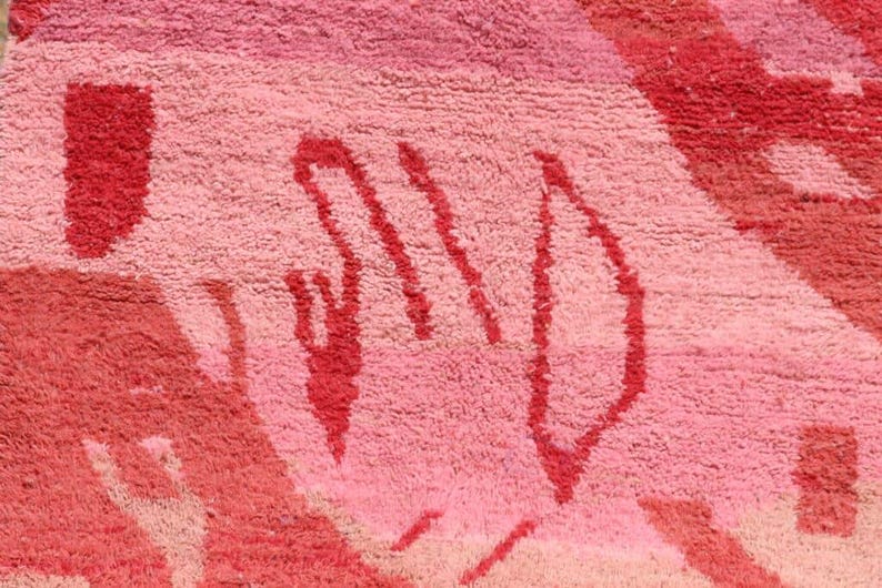 May include: Close-up of a pink and red rug with a textured surface. The rug features abstract shapes in varying shades of pink and red, creating a vibrant and artistic design. The rug's design is a mix of geometric and organic forms.