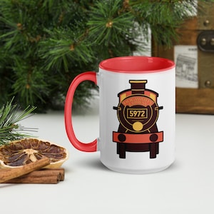 Op de afbeelding: Een witte keramische mok met een felrode binnenkant en handvat. De voorzijde is voorzien van een grafische illustratie van een donkerbruine stoomlocomotief met de tekst Hogwarts Express en het nummer 5972 op een geel en bruin embleem.