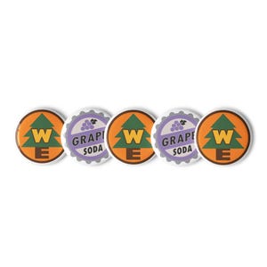 May include: A set of five circular pin-back buttons arranged in a row. Three buttons feature an orange background with a green pine tree and the letter W in yellow. Two buttons feature a light purple background with a grape cluster icon and the text GRAPE SODA in black.