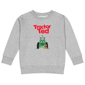 以下が含まれることがあります： グレーの長袖スウェットシャツ。赤い文字で「Tractor Ted」と書かれ、その下に笑顔の緑色のトラクターと、その前に座る小さな茶色の犬のグラフィックが描かれています。トラクターのナンバープレートには「TED 1」と記されています。