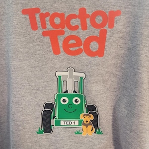 May include: A heather gray sweatshirt featuring the red text Tractor Ted above a graphic of a green cartoon tractor with a smiling face and a license plate reading TED 1, accompanied by a small brown and black dog sitting in green grass.