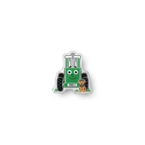 May include: A die-cut sticker featuring a green cartoon tractor with a smiling face, black tires, and a grey exhaust pipe. The tractor has a white license plate that reads TED 1. A small brown and black dog sits in front of the tractor on green grass.