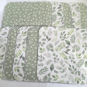 May include: A set of ten square baby washcloths. The washcloths feature two different patterns: a light green dotted pattern and a white background with green leaf patterns. The edges are finished with a gray stitch.