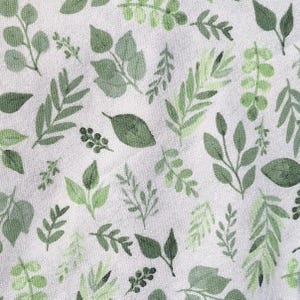 May include: A white fabric with a repeating pattern of green leaves and branches. The leaves are in various shapes and sizes, and the branches are thin and delicate. Spring cleaning must haves farmhouse kitchen decor reusable cotton unpaper towels eco friendly dishcloths plastic free home cleaning swap zero waste home essentials handmade sustainable housewarming gift kitchen swap green home Plant lover kitchen accessories monsters leaves Florida inspired green Kitchen style plant theme