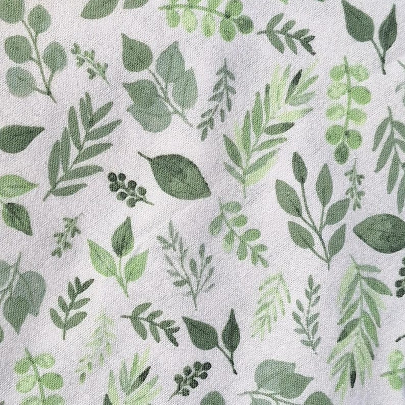 May include: A white fabric with a repeating pattern of green leaves and branches. The leaves are in various shapes and sizes, and the branches are thin and delicate. Spring cleaning must haves farmhouse kitchen decor reusable cotton unpaper towels eco friendly dishcloths plastic free home cleaning swap zero waste home essentials handmade sustainable housewarming gift kitchen swap green home Plant lover kitchen accessories monsters leaves Florida inspired green Kitchen style plant theme