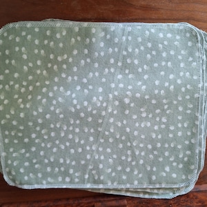 May include: A stack of light green fabric cloths with a white polka dot pattern. The cloths are folded and have a stitched edge.