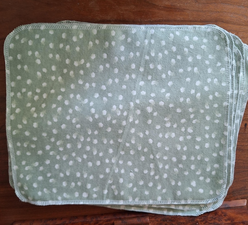 May include: A stack of light green fabric cloths with a white polka dot pattern. The cloths are folded and have a stitched edge.