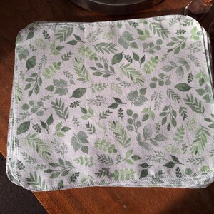 May include: A stack of white fabric cloths with a green leafy pattern. The cloths are sewn together with a white thread.