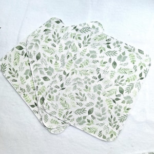May include: Four white cotton cloths with a green leafy pattern. The cloths are folded and stacked on top of each other.