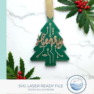 Pode incluir: Enfeite de Natal verde em forma de árvore, com detalhes dourados e o nome "Henry" em itálico. O design incorpora um circuito impresso e uma fita dourada. O texto "SVG LASER READY FILE" é visível na parte inferior.