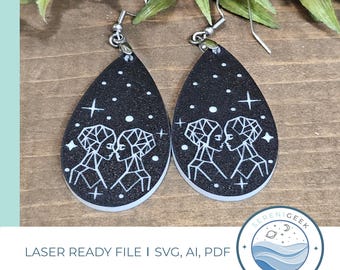 May include: A pair of black teardrop-shaped earrings with a white geometric design of two figures facing each other. The earrings have a sparkly black background with white stars.